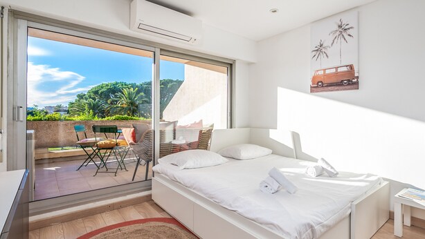 A modern bedroom with a large bed, a glass door leading to a balcony, and a view of greenery.