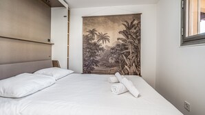 A modern bedroom with a large bed, a headboard, a tapestry depicting a tropical scene, and a window with blinds.