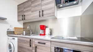 A modern kitchen with wooden cabinets, a stainless steel oven, a red coffee maker, and a built-in microwave.