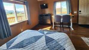 A bedroom with a bed, a desk with two chairs, a TV, and a door. - Circle R Cabin 1, Private Ranch, Mountain Views (East Glacier Park Village)