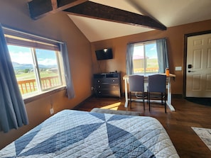 A bedroom with a bed, a desk with two chairs, a TV, and a door.