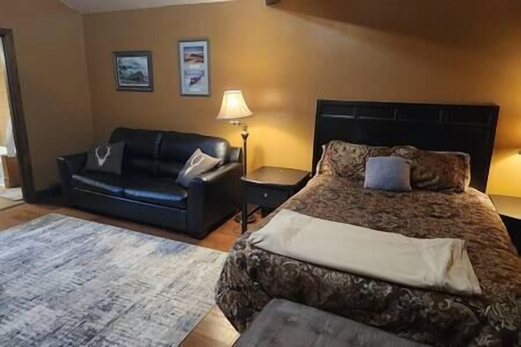 A bedroom with a bed, a black sofa, a nightstand, and a lamp.
