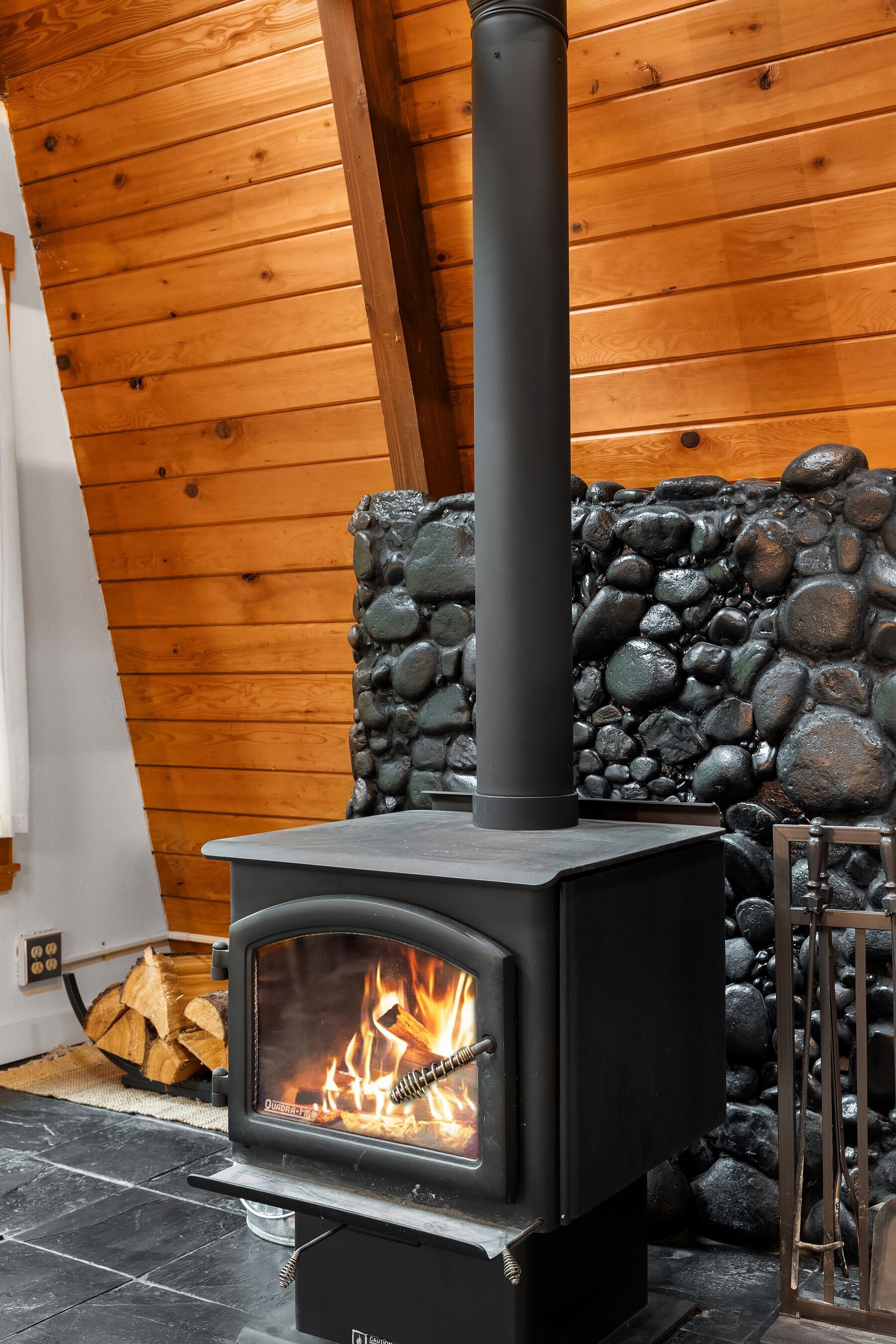 Un poêle à bois, avec un mur en pierre en arrière-plan et un plafond en bois.