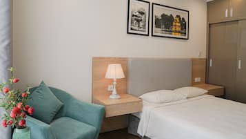 A hotel room with a bed, a nightstand with a lamp, a chair, and two framed pictures on the wall.