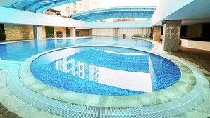 Une vaste piscine intérieure dotée d’un toit en verre, entourée d’un bâtiment moderne à plusieurs niveaux et agrémenté de balcons.