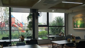 Une salle de conférence équipée de tables et de chaises, de grandes fenêtres donnant sur un terrain de jeux et sur la verdure, et d’un ventilateur de plafond.