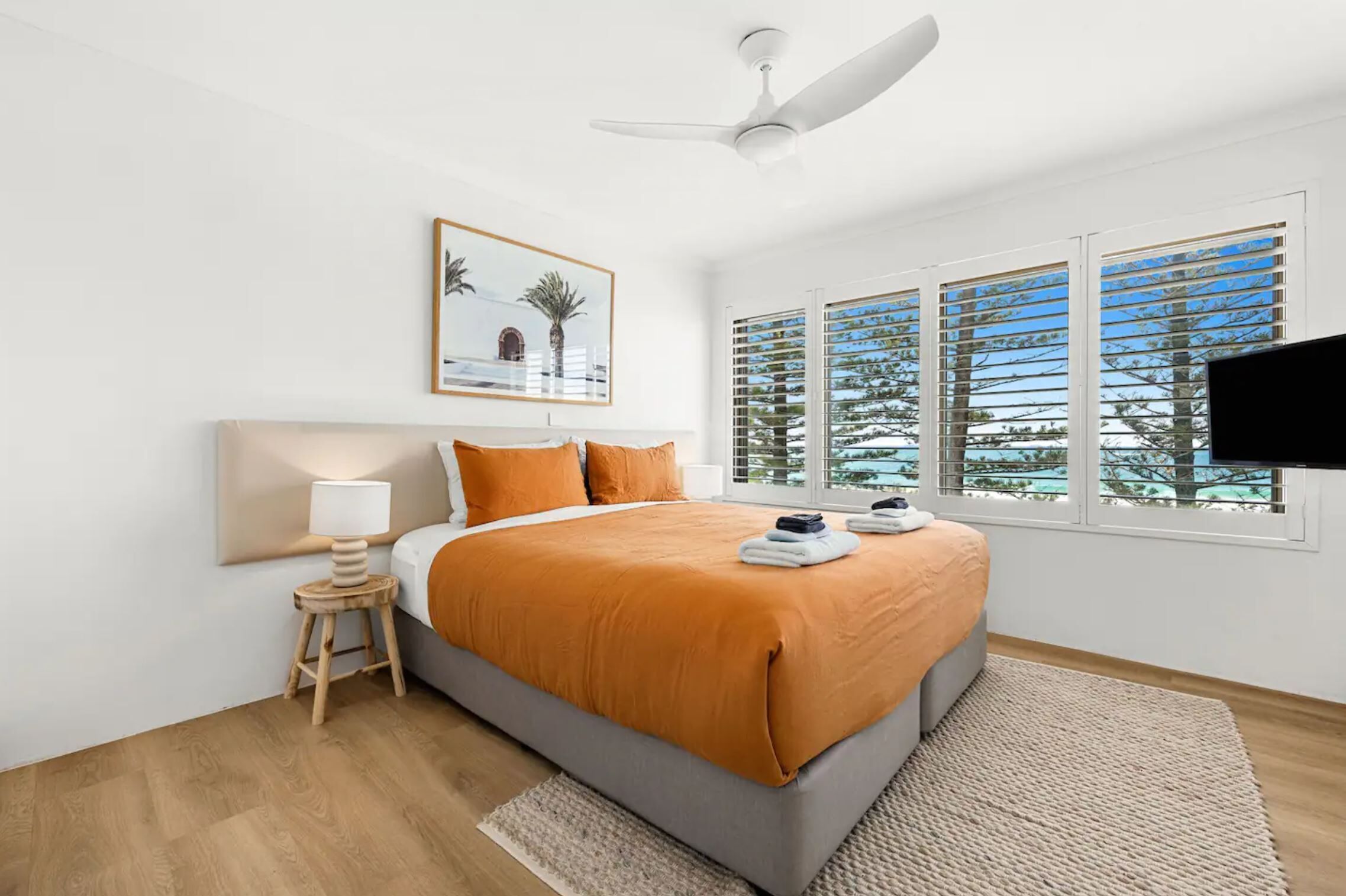 A modern hotel room with a large bed, a ceiling fan, a TV, and a window with a view of trees and a building.