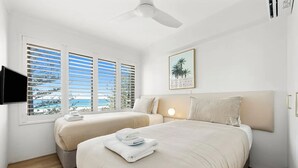 Ein Hotelzimmer mit zwei Betten, einem Deckenventilator, einem an der Wand montierten Fernseher und einem Fenster mit Jalousien.