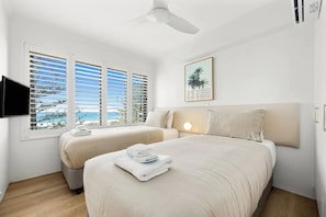 A hotel room with two beds, a ceiling fan, a TV mounted on the wall, and a window with blinds. - Beachfront living & ocean views (Buddina)
