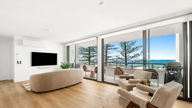 Ein modernes Wohnzimmer mit großem Fernseher, bequemen Sitzgelegenheiten und einem Balkon mit Meerblick.