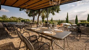 Un espace de restauration en plein air, avec des tables pour deux, entourées de chaises, sous un toit abrité agrémenté d’un lustre.