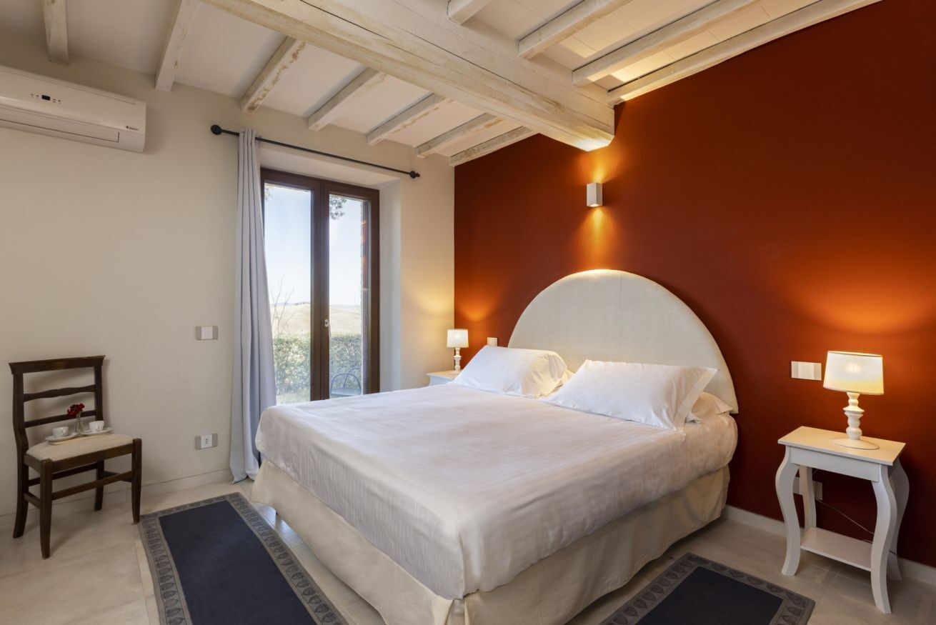 Un dormitorio con una cama grande, una silla, una mesita de noche y una ventana con cortinas.