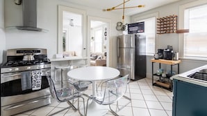 A modern kitchen with a stainless steel stove, a refrigerator, and a dining area with a white table and clear chairs. - Modern + Spacious 5BR/2BA Home, Renovated Backyard (Bridgeport)