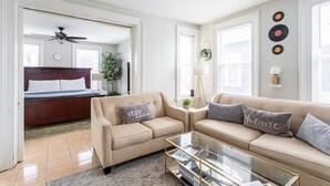 A modern living room with a sofa, coffee table, and a bed in the background. - Modern + Spacious 5BR/2BA Home, Renovated Backyard (Bridgeport)