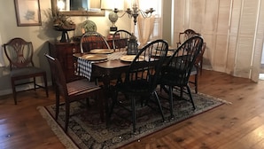 Un comedor con una mesa de madera dispuesta para seis personas, rodeada de sillas. Hay una araña sobre la mesa y un espejo en la pared.