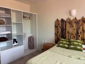 A bedroom with a bed, a wardrobe, a bedside table, a wall-mounted fan, and a bamboo wall decoration. - Modern House, Upscale Mexican neighborhood. (Oaxaca)