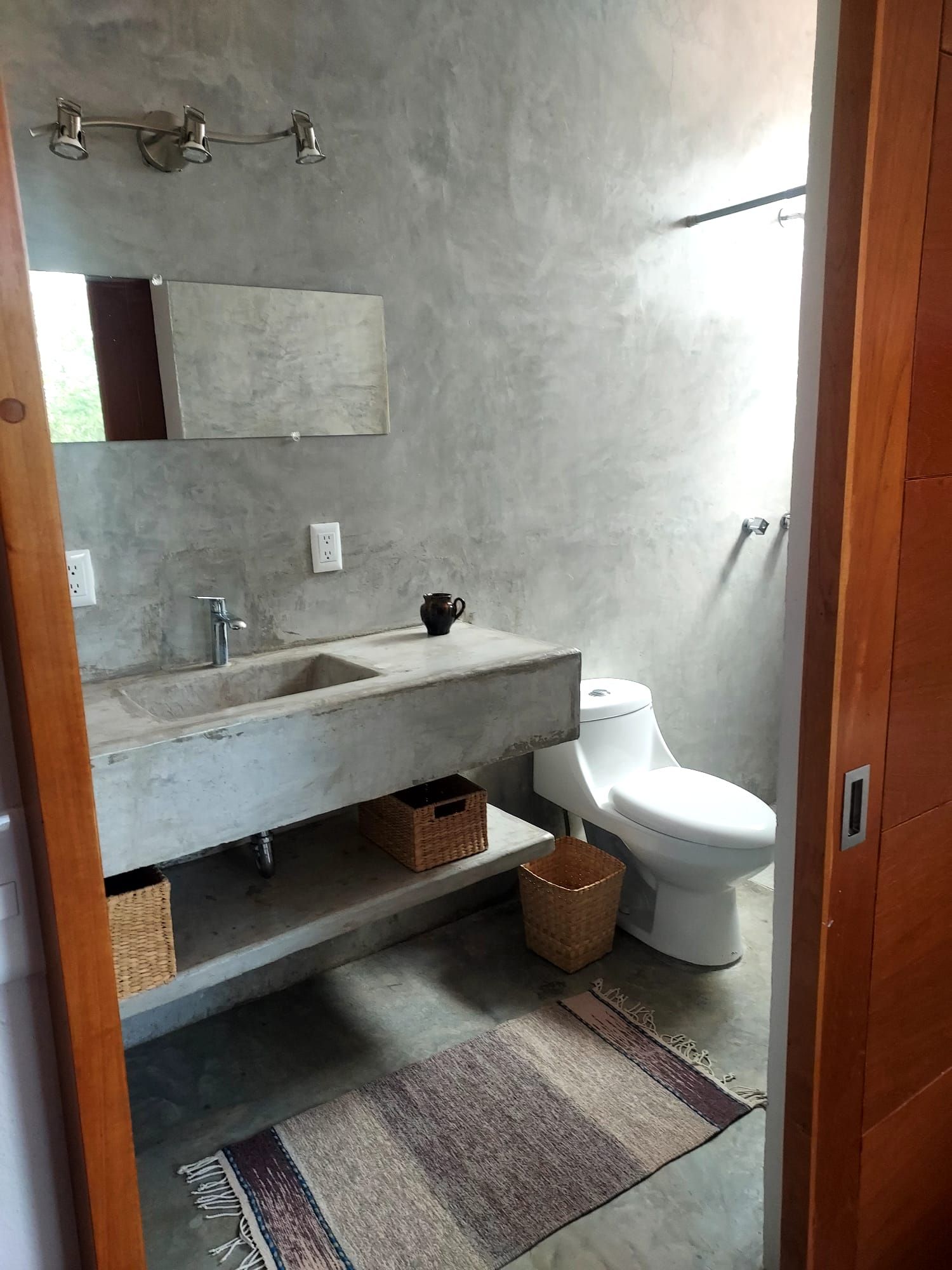 A bathroom with a concrete sink, a white toilet, and a shower area.