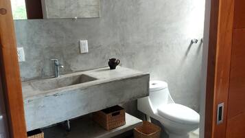 A bathroom with a concrete sink, a white toilet, and a shower area.