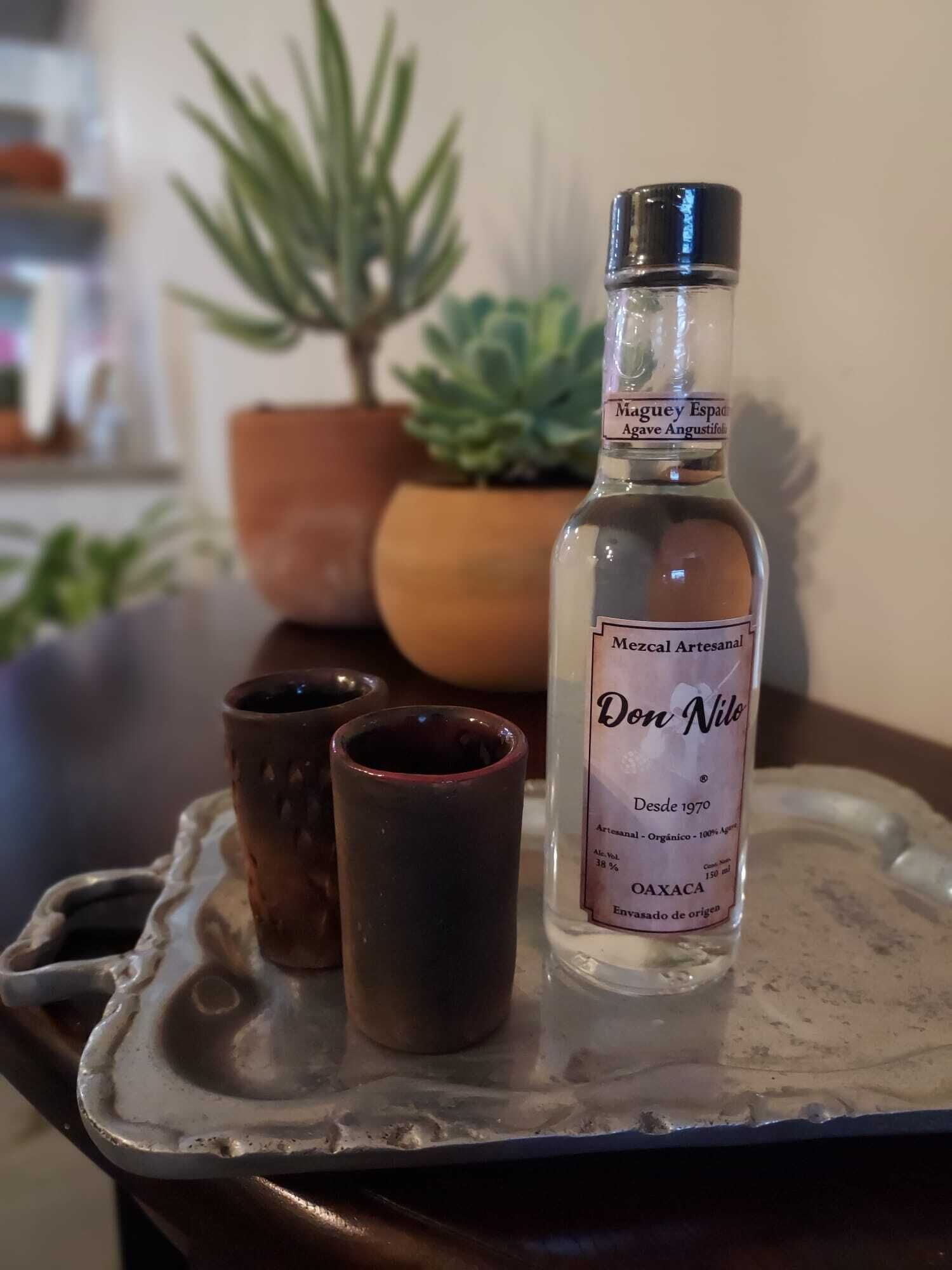 Eine Flasche Don Nilo Mezcal auf einem Tablett mit zwei kleinen Gläsern.