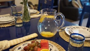 Une table à manger dressée avec des assiettes, une carafe d’eau, un vase de fleurs jaunes et un saladier de fruits.
