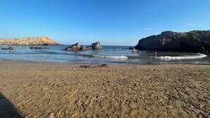 Ein Sandstrand mit Felsen und blauem Himmel.