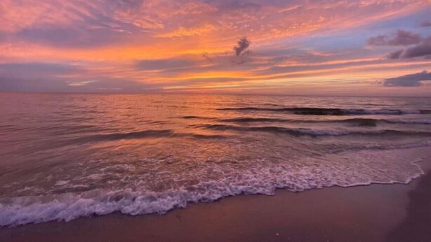 Une plage avec des vagues et un coucher de soleil.
