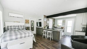 Une chambre moderne avec un lit, un petit coin cuisine doté d’un comptoir et de tabourets, et un espace de vie avec un canapé et des fauteuils.
