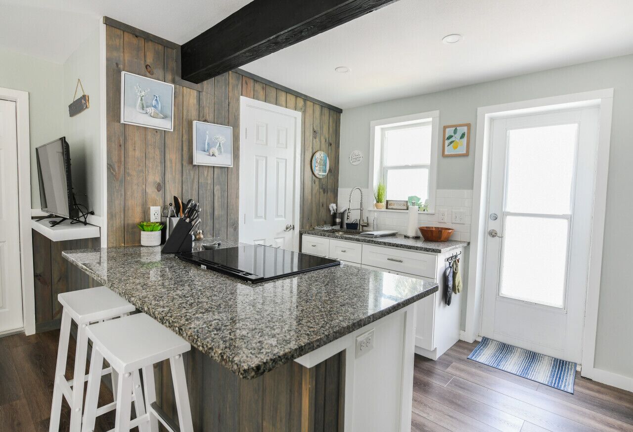Eine Küche mit Granitarbeitsplatte, weißen Schränken und einer Wand in Holzoptik.