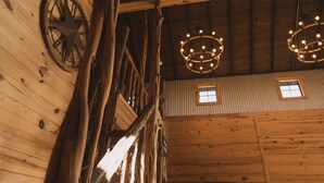 A rustic interior with wooden beams, a large wheel, and two chandeliers. - 3 Chicks Ranch, 2 Cabins, Pool, Hot Tub & Hill Country (New Braunfels)