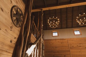 A rustic interior with wooden beams, a large wheel, and two chandeliers. - 3 Chicks Ranch, 2 Cabins, Pool, Hot Tub & Hill Country (New Braunfels)