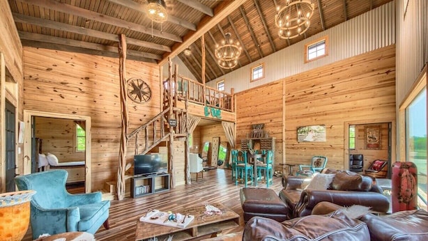 A spacious log cabin interior with a wooden staircase, leather sofas, and a cozy seating area. - 3 Chicks Ranch, 2 Cabins, Pool, Hot Tub & Hill Country (New Braunfels)