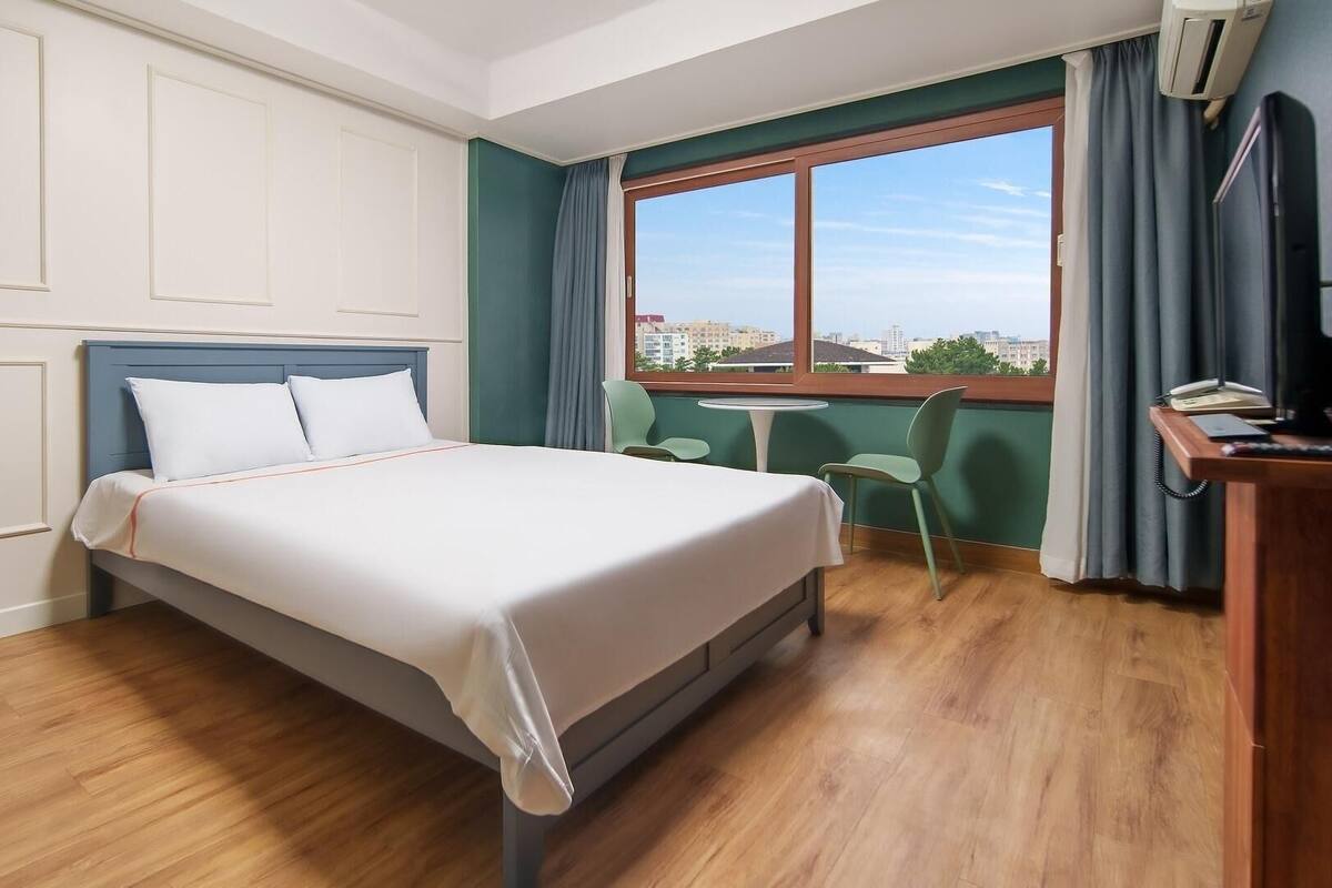 Ein Hotelzimmer mit Bett, Schreibtisch, Stuhl, einem kleinen Tisch und einem Fenster mit Blick.