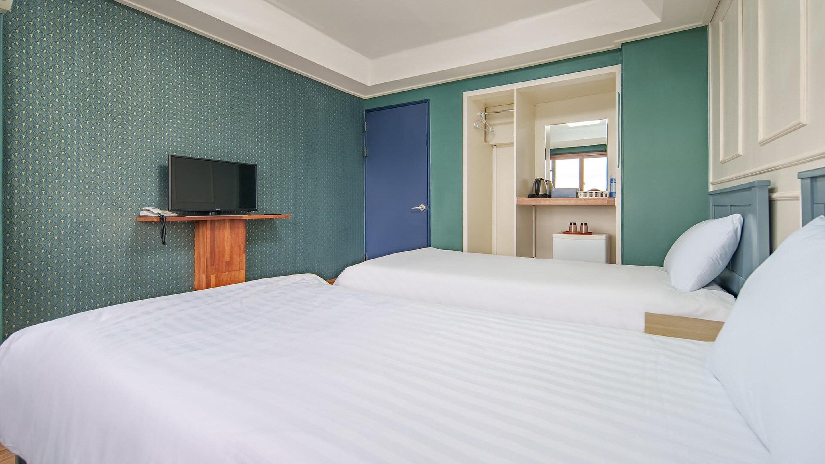 A hotel room with two beds, a television on a wooden stand, and a bathroom visible through an open door.