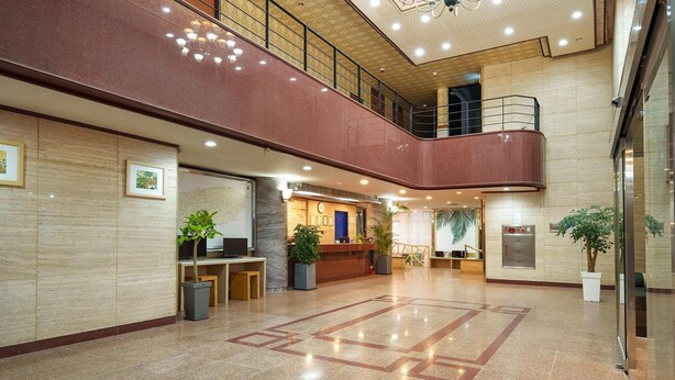 Een ruime lobby met een receptiebalie, twee liften en een trap naar een hoger niveau.