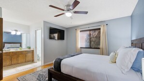 A bedroom with a bed, a ceiling fan, a window with curtains, a wooden headboard, and a bathroom visible in the background. - Hot tub, Game Room, Outdoor Kitchen & much more! (Visalia)