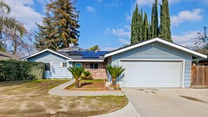 A single-story house with a garage, solar panels, and a well-maintained lawn. - Hot tub, Game Room, Outdoor Kitchen & much more! (Visalia)
