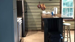 A kitchen with a refrigerator, a wooden wall, a welcome sign, a clock, and a window.