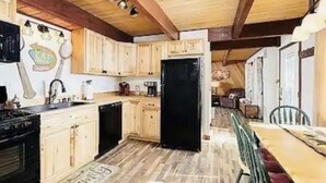 Cuina amb armaris de fusta, un refrigerador negre i una taula de dinar amb cadires.