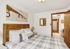 A bedroom with a wooden headboard, a bed with a plaid bedspread, and a wall-mounted mirror.
