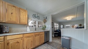 Una cocina con armarios de madera, encimera de granito, un lavabo y un cubo de basura.