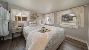 Un dormitorio con cama, mesitas de noche, cortinas y vistas al exterior.