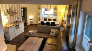 A living room with a sofa, coffee table, and dining area with chairs. - Holiday Home 'Anker Perla' with Private Terrace and Wi-Fi (Grömitz)