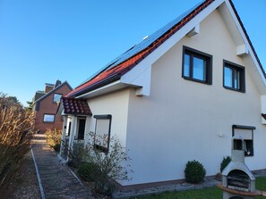A modern two-story house with a sloped roof, a brick chimney, and a small garden area with a barbecue grill.
