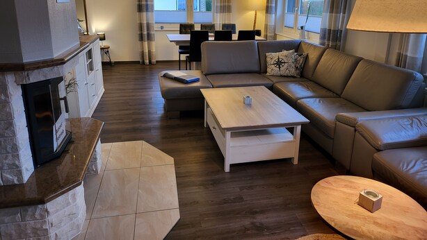 A living room with a fireplace, a sofa, a coffee table, and a dining area in the background. - Holiday Home 'Anker Perla' with Private Terrace and Wi-Fi (Grömitz)