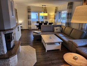 A living room with a fireplace, a sofa, a coffee table, and a dining area in the background.