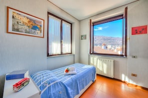 Une chambre avec un lit, une fenêtre donnant sur un beau paysage, un radiateur et une petite table sur laquelle est posé un train jouet.
