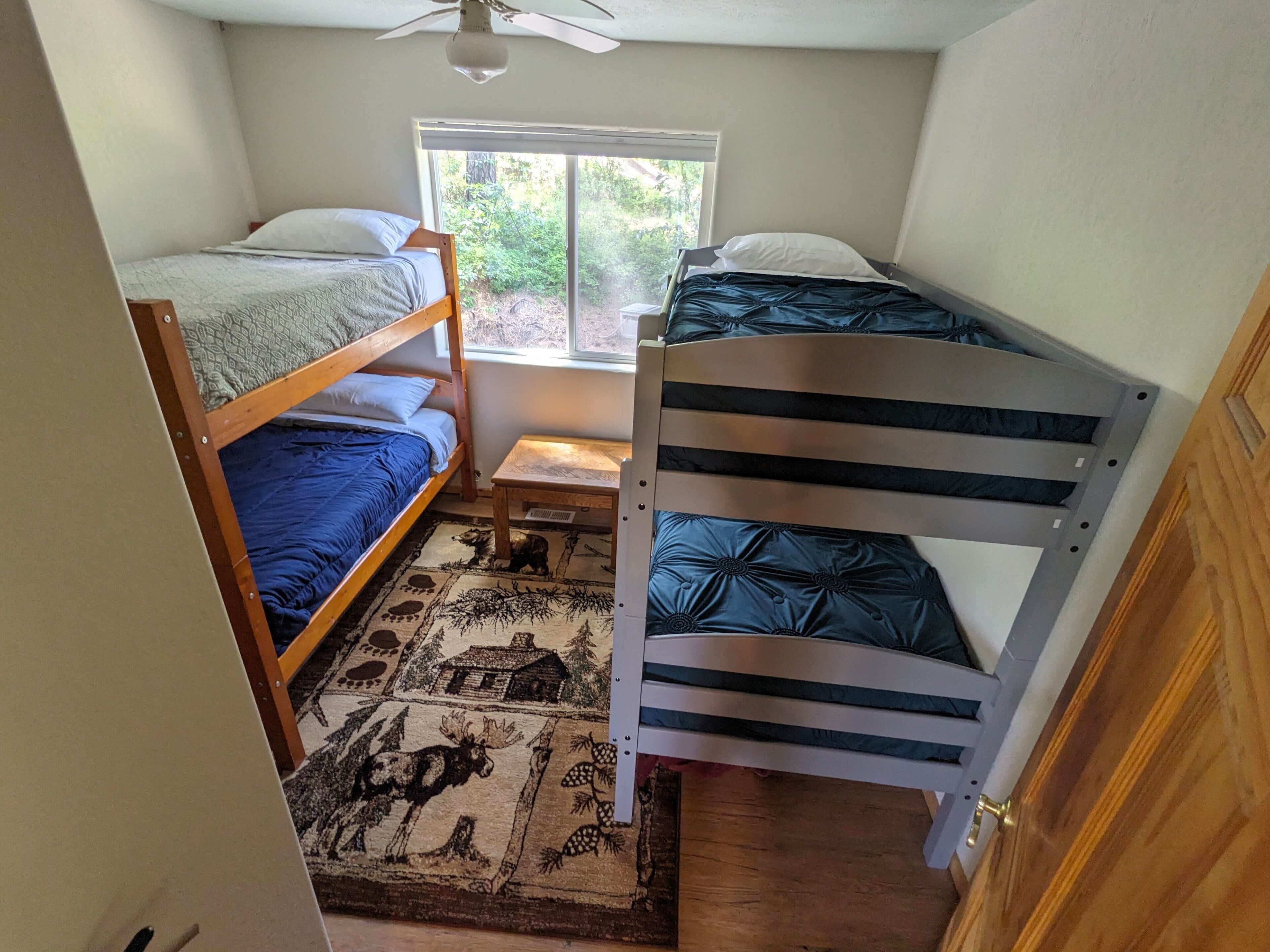 A small room with two bunk beds, a window, a ceiling fan, and a rug with animal prints.