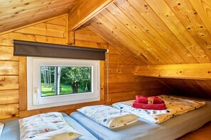 Une cabane en bois avec une fenêtre, un lit recouvert d’une courtepointe à pois et une serviette rouge.
