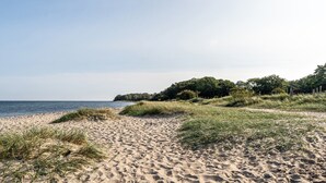 Una playa arenosa con dunas cubiertas de hierba y una vista despejada del mar.