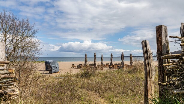 A beach with wooden chairs and umbrellas, a covered area, and a wooden fence.